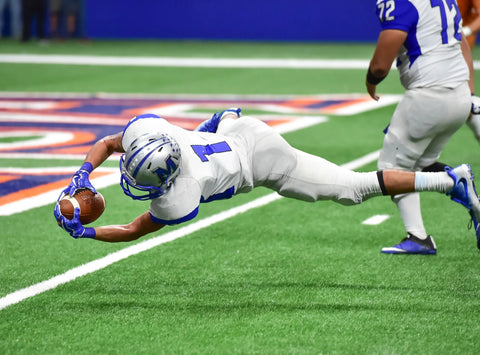 Football player diving to catch ball in end zone during game, athletic action shot