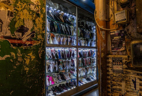 A glass display case filled with various colorful sneakers in a rustic urban setting.