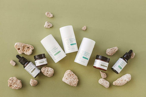 Nora CBD topicals including cream, oil, and balm arranged with natural stones on a green background.