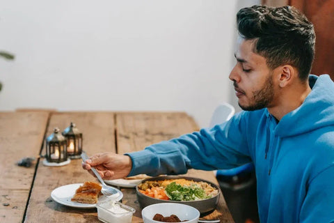 A young man in a blue hoodie enjoying a meal of CBD-infused edibles at a wooden table.