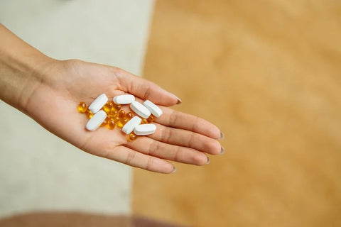 A person's hand holding a mix of white pills and yellow softgel supplements.
